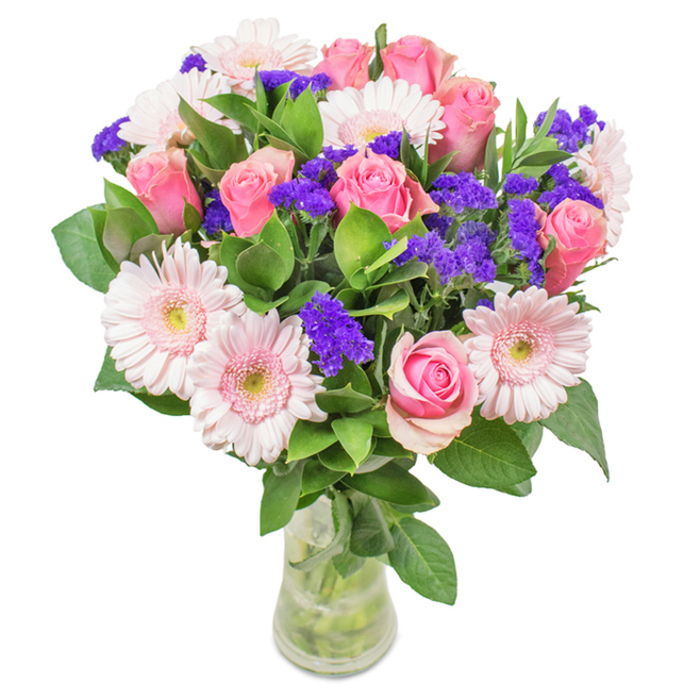 An elegantly calibrated bouquet unfolds in a clear glass vase set before a pristine white backdrop-its heart composed of approximately seven to nine soft-to-medium pink roses, the petals either tightly furled or just beginning to uncurl with their classic, inviting spirals. Intertwined among them are five to seven pale pink Gerbera daisies, easily identifiable by their broad faces and rings of delicate petals, their centers subtly fading to a creamy white. Punctuating this symphony of pinks are vivid, textural clusters of deep purple statice, which provide an energizing, almost whimsical contrast, much like bursts of color seen in the flower stalls of Stockwell Market. Rich, dark-green foliage weaves beneath and among the blooms, creating visual abundance and enhancing the overall lushness. Each visible stem rests in the vase's cool water, the transparency adding to the sense of freshness and care. This arrangement, ideal for gifting on birthdays, anniversaries, Mother's Day, or as a sophisticated enhancement for a Stockwell workspace or home, conveys an aura of celebration and refined joy-a floral expression crafted with heart and local understanding.